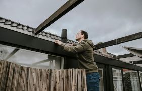 Een man inspecteert zijn dakgoot op mogelijke lekkages.