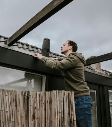 Een man inspecteert zijn dakgoot op mogelijke lekkages.