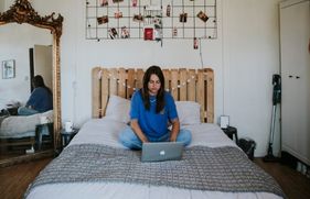 Een jonge vrouw zit op haar bed. Ze is online aan het shoppen op haar laptop.