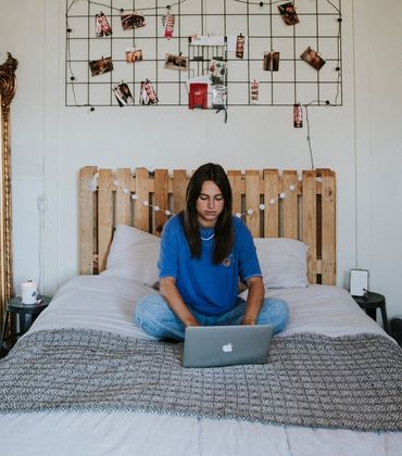 Een jonge vrouw zit op haar bed. Ze is online aan het shoppen op haar laptop.