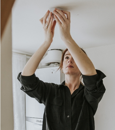 Een vrouw bevestigt een rookmelder aan het plafond