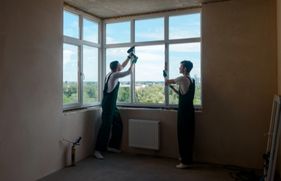 2 mannen in werk-overalls verrichten isolatiewerkzaamheden aan een raam.