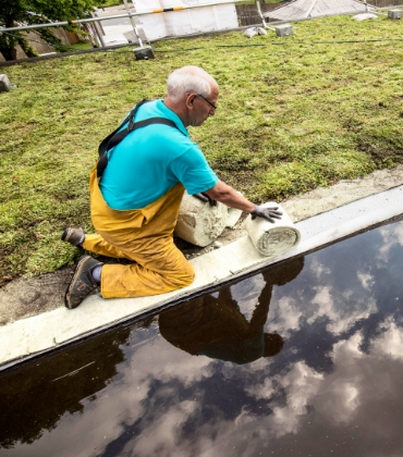 Een man zit op zijn knieën en is een dak aan het verduurzamen.