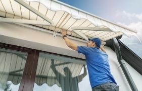 Man met pet op maakt zonwering schoon