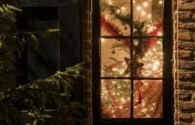 Raam van een woning waardoor een versierde kerstboom te zien is