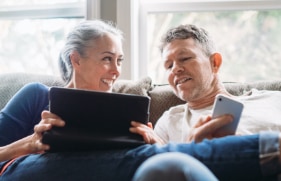Man en vrouw die op de bank zitten en op hun tablet en smartphone bezig zijn