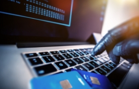 Een hand met een handschoen typt op een toetsenbord waar bankpasjes op liggen