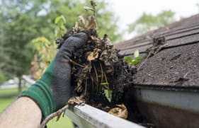 Hand met werkhandschoen die troep uit de dakgoot verwijdert