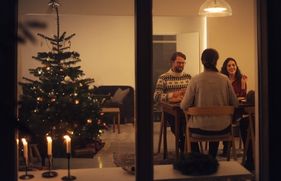 4 mensen zitten binnenshuis aan een keukentafel, naast een rijkversierde kerstboom.