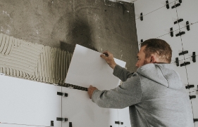 Een man plaatst witte wandtegels tegen de muur.