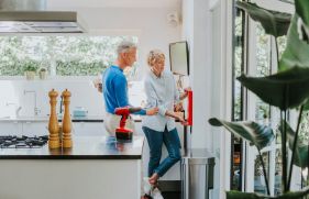 Een man en een vrouw bevestigen samen een blusdeken aan de muur in de keuken.