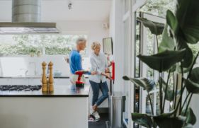 Een man en een vrouw staan in de keuken, en hangen samen een blusdeken aan de wand.