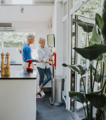 Een man en een vrouw staan in de keuken, en hangen samen een blusdeken aan de wand.