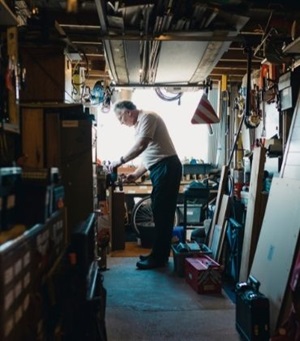 Oudere man staat in zijn schuur te werken aan de werkbank