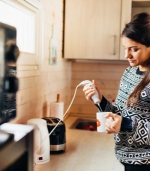 Vrouw in keuken met staafmixer. Lees hoe je de kans op kortsluiting en elektriciteitsschade in huis verkleint.